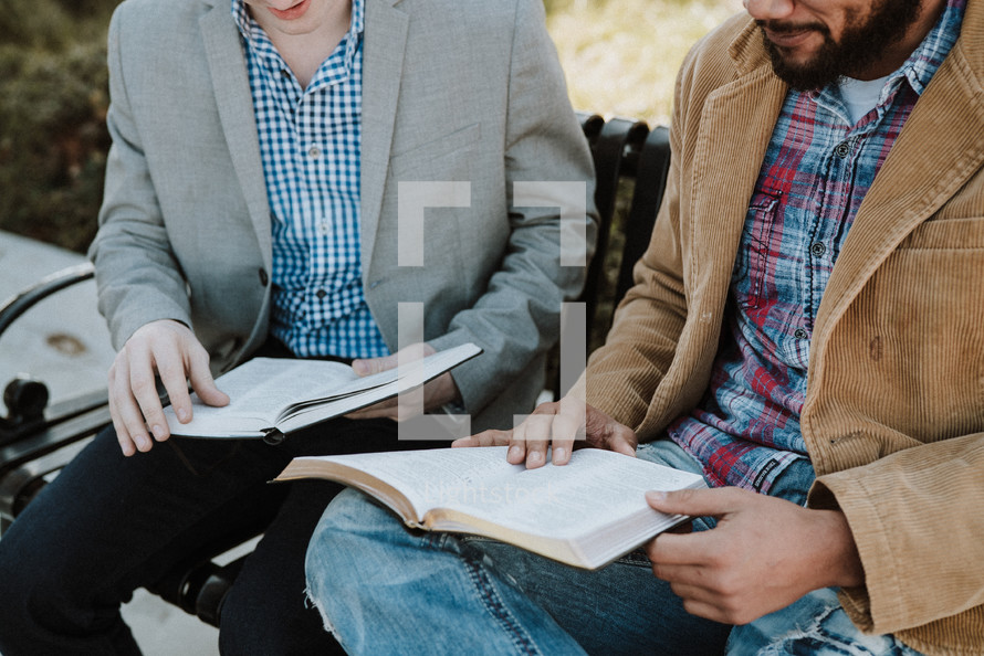 two men reading scripture sitting on a park bench 