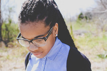 an African American teen girl in reading glasses looking down 