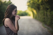 teen girl standing in the middle of a rural road praying 