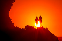 women standing at the edge of a cliff at sunset under the glow of a vibrant sky