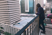 woman standing on a balcony looking out at the city below 