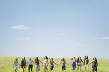 Teen girls holding hands, running through a field.