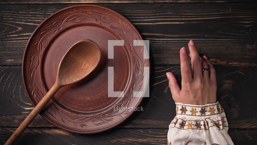Ukrainian woman sitting in national restaurant and waiting for order. Girl knocks fingers nervously on wooden table while waiting for dish. Empty clay plate with spoon.