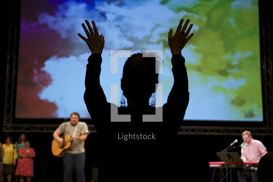 a woman with raised hands and worship leaders leading a congregation in song 
