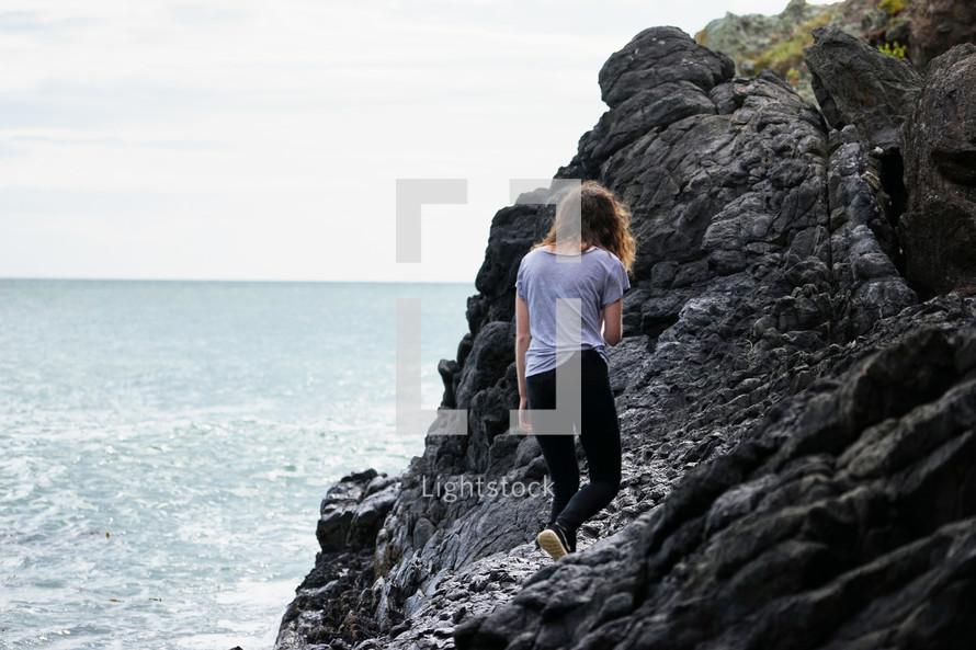 young woman walking on rocky shoreline 