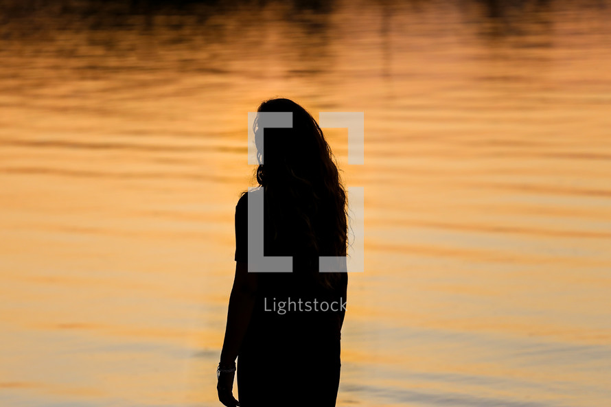 silhouette of a woman standing in front of water at sunset 