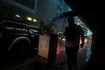 a man carrying an umbrella walking on a city sidewalk in the rain 
