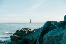 rocks on a beach and a distant lighthouse 