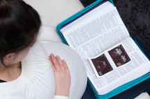 pregnant mother looking at ultrasound photos on a Bible 