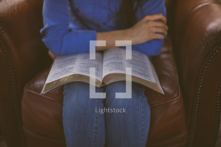 A woman sitting in a chair with an open Bible in her lap
