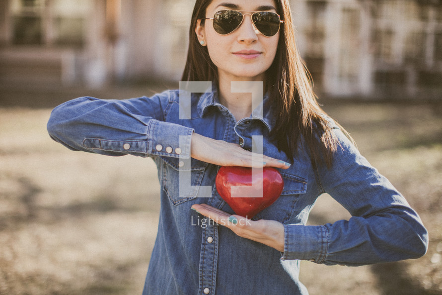 A young woman wearing sunglasses and holding a red heart