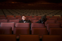 man in a tuxedo sitting in an empty auditorium 