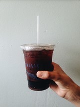 a hand holding a plastic cup full of soda 