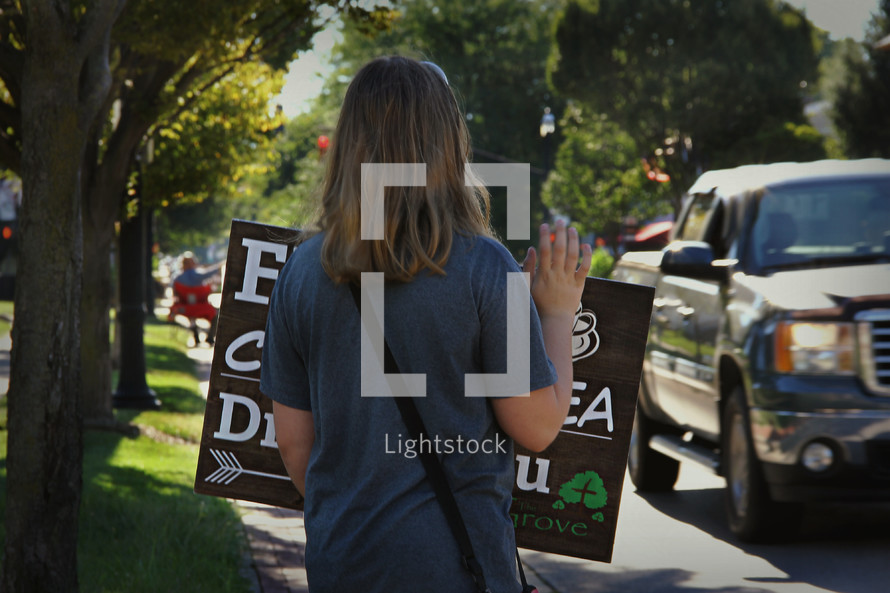 teens holding signs greeting cars driving by 