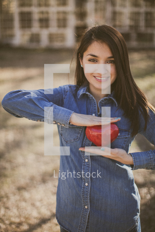 A smiling young woman holding a red heart