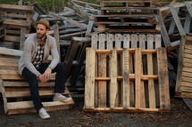 a man sitting next to a pile of old pallets 