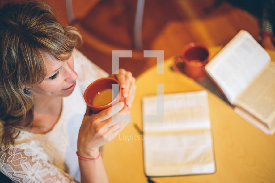 Woman drinking a cup of coffee, an open bible on the table in front of her