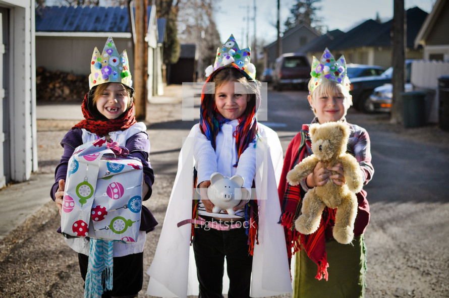 children dressed as the three kings a holding Christmas gift, teddy bear, and piggy bank 