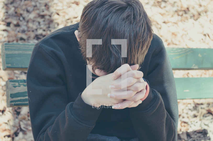  a teen boy with head bowed praying 