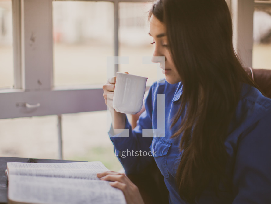 A woman drinking coffee while reading a Bible 