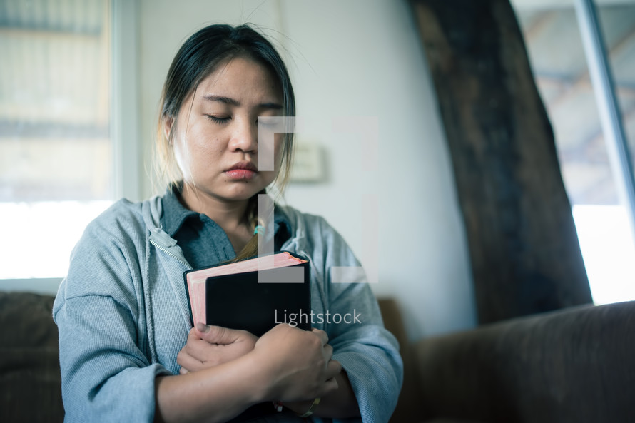 Woman praying with bible in a room. 