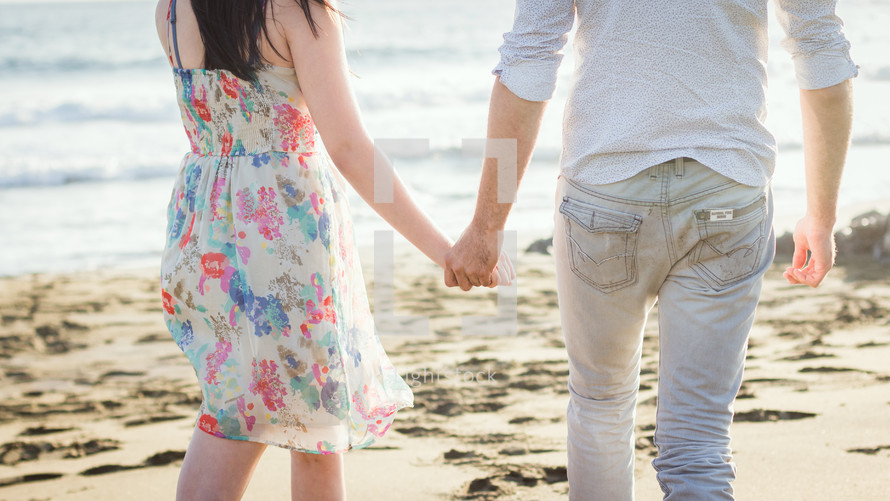 a couple walking on a beach holding hands 