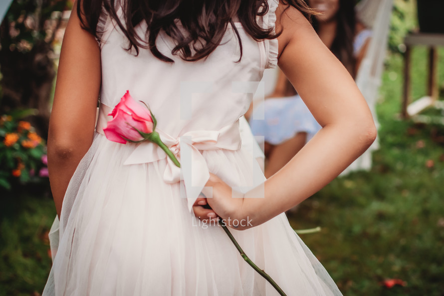 a girl holding a rose behind her back 