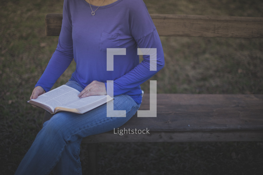 A woman sitting on a bench reading the Bible