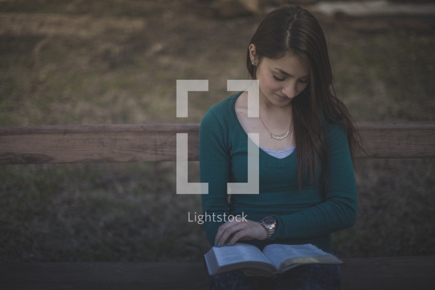 A young woman sitting on a bench reading the Bible