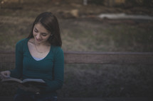 A young woman smiling and reading the Bible on a bench