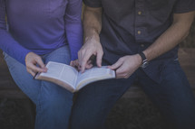 A man and woman sitting on a bench reading the Bible together