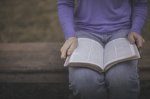 A woman sitting on a bench reading a Bible