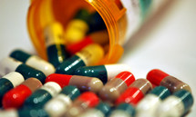 Bright colored medicine capsules spilling from a prescription container.