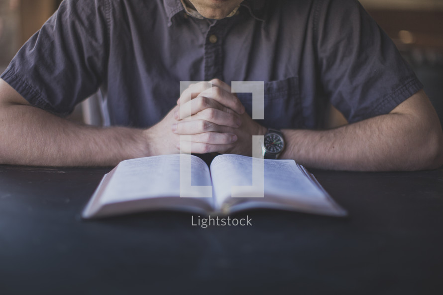 A man with hands folded in front of a Bible