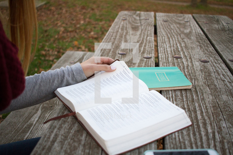 a woman reading a Bible at a picnic table in fall 