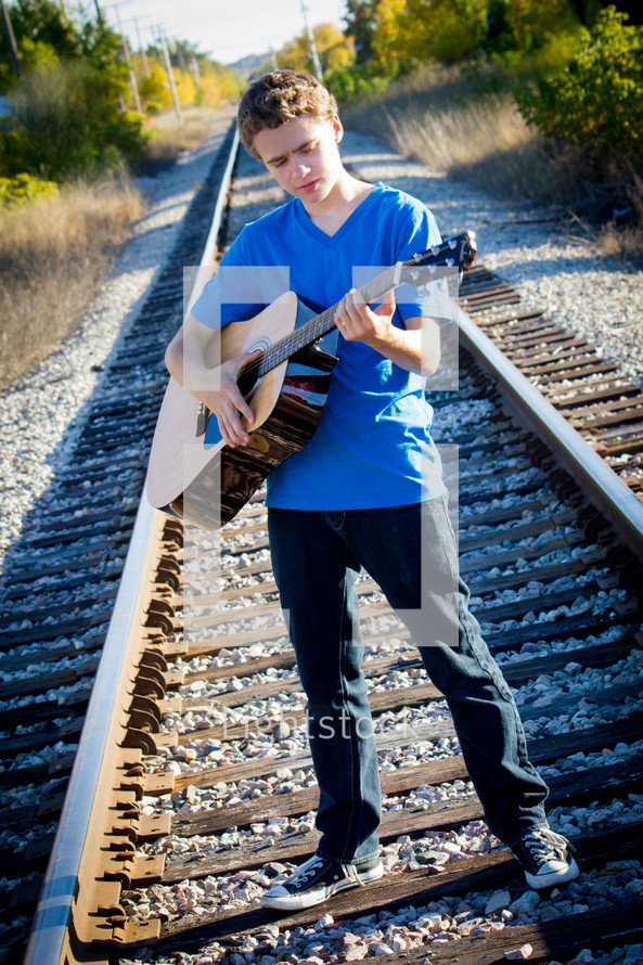 teen boy playing a guitar on railroad tracks 