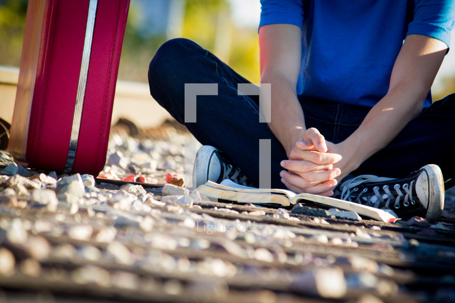 man sitting on the ground praying with a Bible 