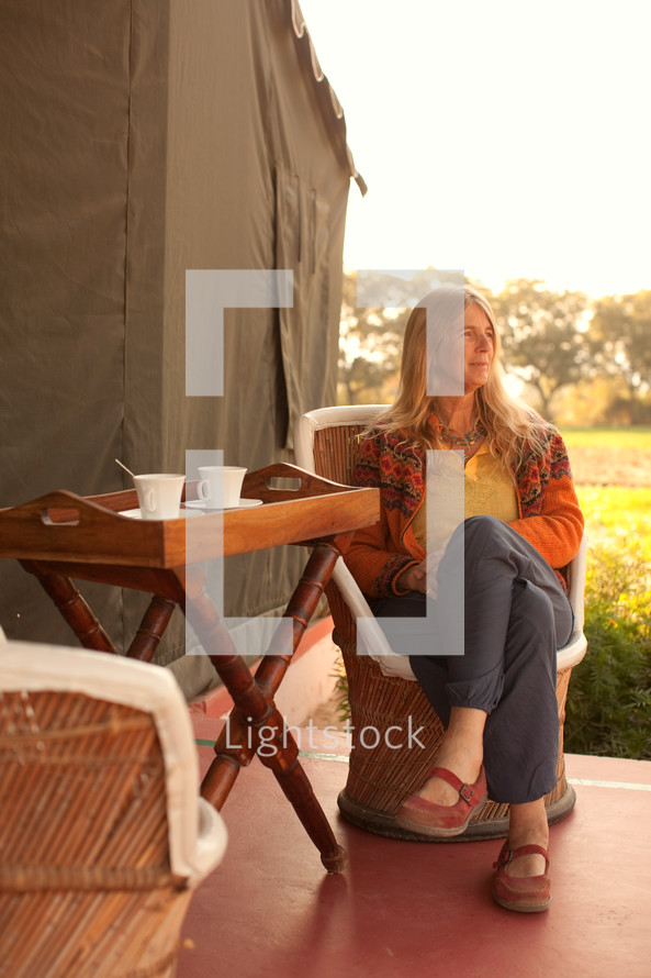 a woman sitting in a chair drinking tea next to a tent