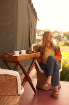 a woman sitting in a chair drinking tea next to a tent