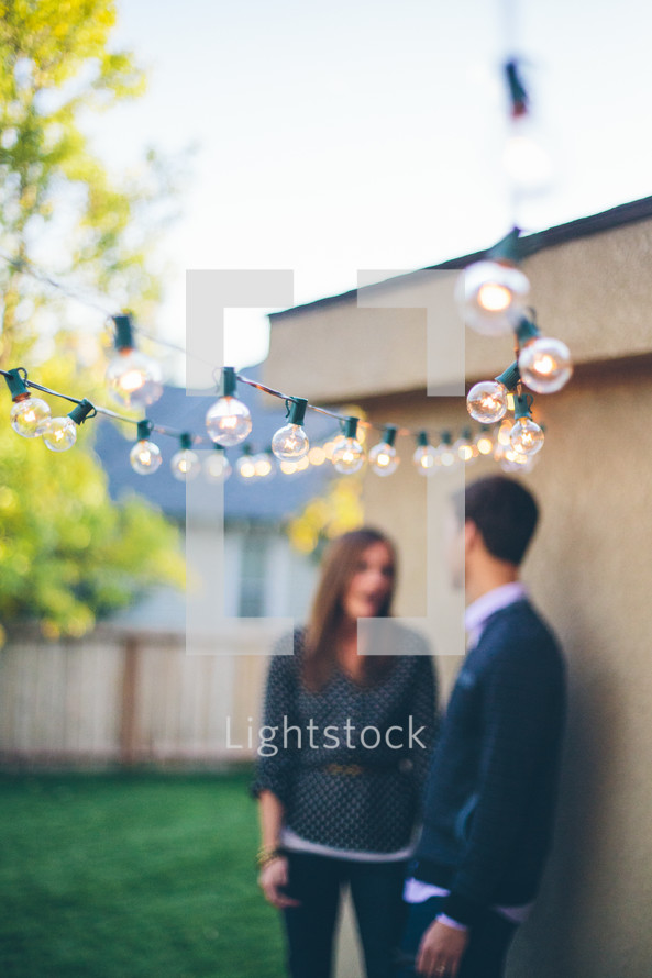Blurry shot of a couple outdoors, standing under a string of lights 