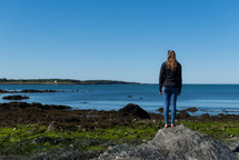 a woman standing on a rocky shore 