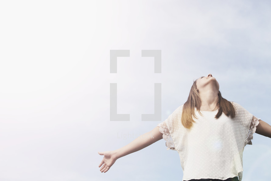 Young teenage girl with arms extended looking into the heavens.