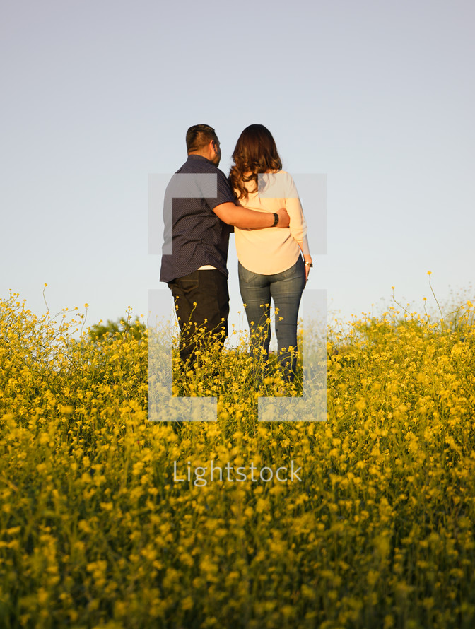 a couple standing in a field of yellow wildflowers 