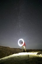 A man making a circle of light under a starry sky.