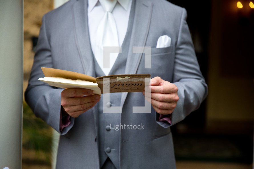 A groom in a grey suit reading a card.