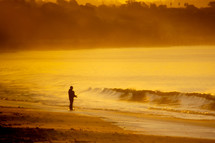 man fishing along a shore at sunset 