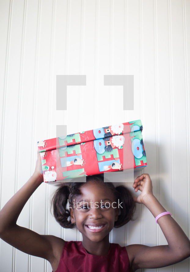 a girl child holding a wrapped Christmas gift over her head 