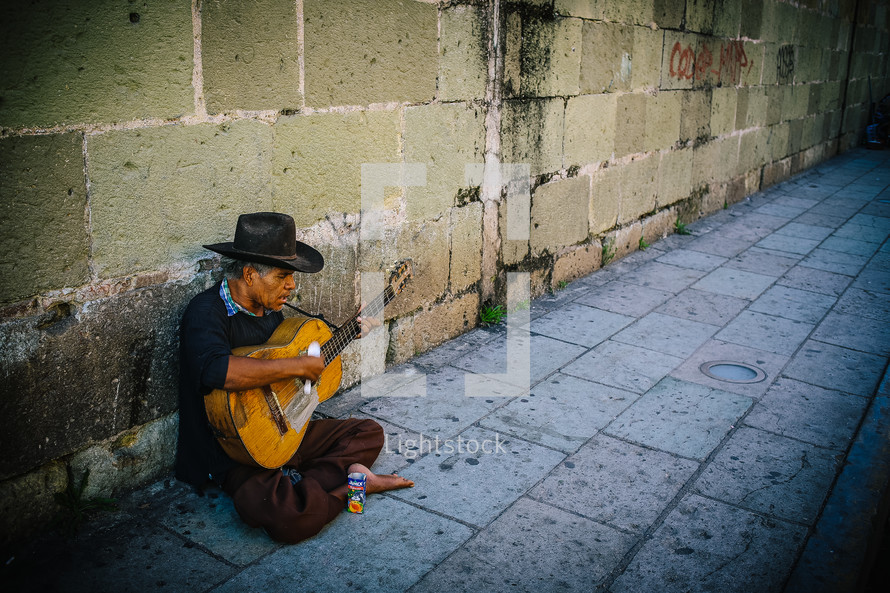 An old man playing a guitar on a stone sidewalk.