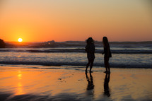 silhouettes of young women standing on a beach at sunset 