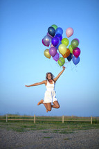 a woman jumping in celebration holding helium balloons 